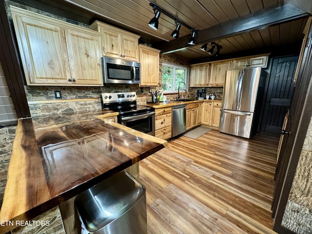 kitchen featuring track lighting, sink, appliances with stainless steel finishes, beam ceiling, and butcher block counters