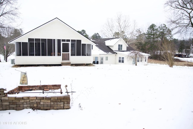 snow covered rear of property with a sunroom