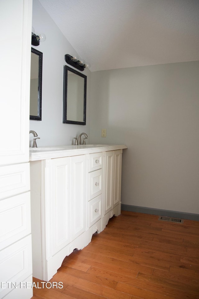 bathroom featuring wood-type flooring, lofted ceiling, and vanity