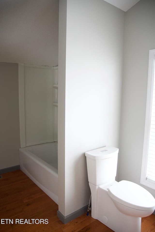 bathroom with a tub to relax in, wood-type flooring, and toilet