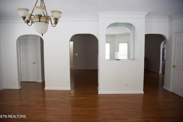 empty room with dark wood-type flooring, crown molding, and a notable chandelier