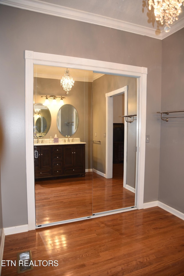 bathroom with an inviting chandelier, vanity, wood-type flooring, and ornamental molding