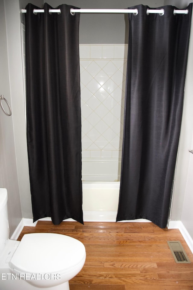 bathroom with shower / bathtub combination with curtain, hardwood / wood-style floors, and toilet