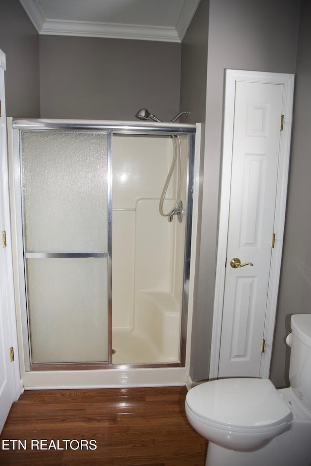 bathroom with wood-type flooring, toilet, crown molding, and a shower with shower door