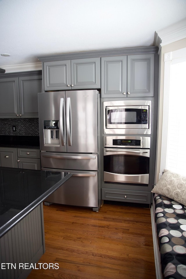 kitchen with gray cabinetry, ornamental molding, dark hardwood / wood-style flooring, stainless steel appliances, and backsplash