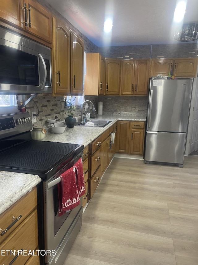 kitchen featuring backsplash, sink, light wood-type flooring, and appliances with stainless steel finishes