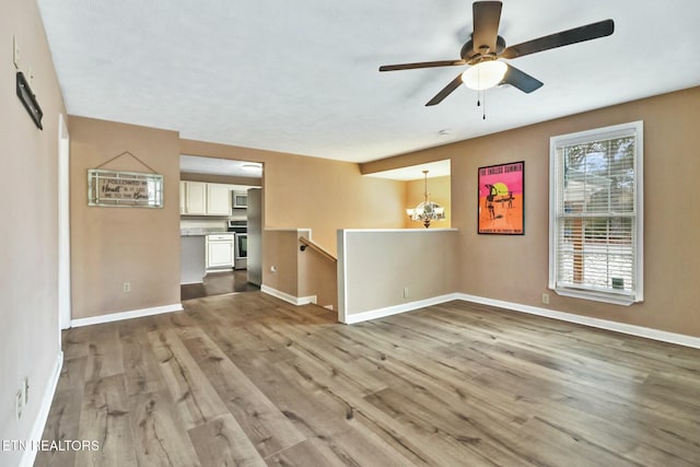 unfurnished living room featuring ceiling fan with notable chandelier and light hardwood / wood-style flooring