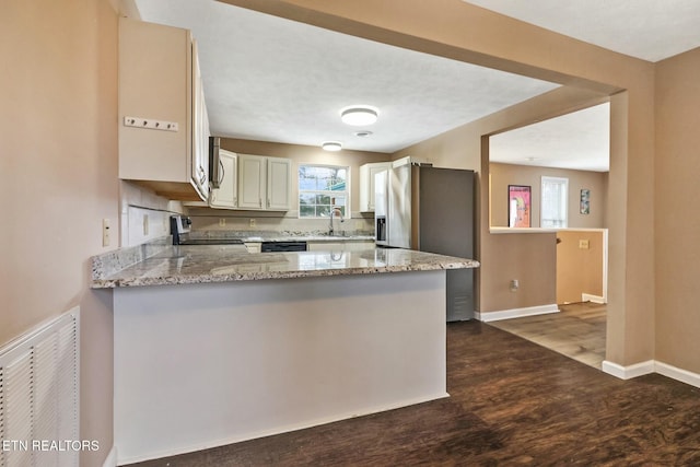 kitchen with light stone countertops, kitchen peninsula, range, and dark wood-type flooring