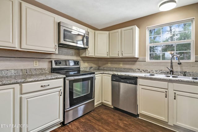 kitchen featuring appliances with stainless steel finishes, dark wood-type flooring, white cabinetry, sink, and backsplash