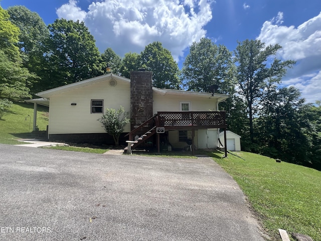 view of front of property featuring a wooden deck, a garage, a front lawn, and an outbuilding