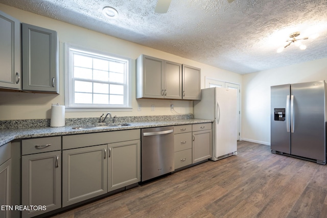 kitchen with sink, a textured ceiling, gray cabinets, appliances with stainless steel finishes, and hardwood / wood-style flooring