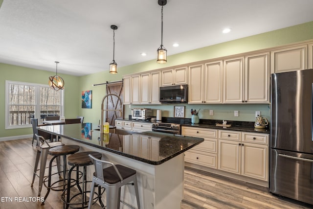 kitchen with a center island with sink, cream cabinets, a barn door, and appliances with stainless steel finishes