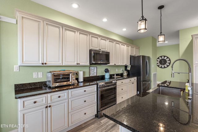 kitchen with appliances with stainless steel finishes, decorative light fixtures, dark stone countertops, and sink