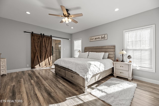 bedroom featuring ceiling fan, multiple windows, a barn door, and wood-type flooring