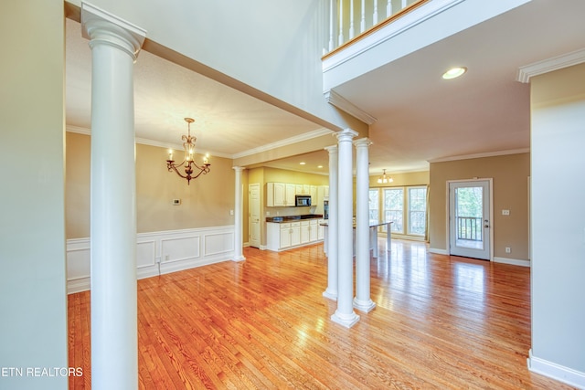 unfurnished living room featuring decorative columns, crown molding, light hardwood / wood-style floors, and a notable chandelier