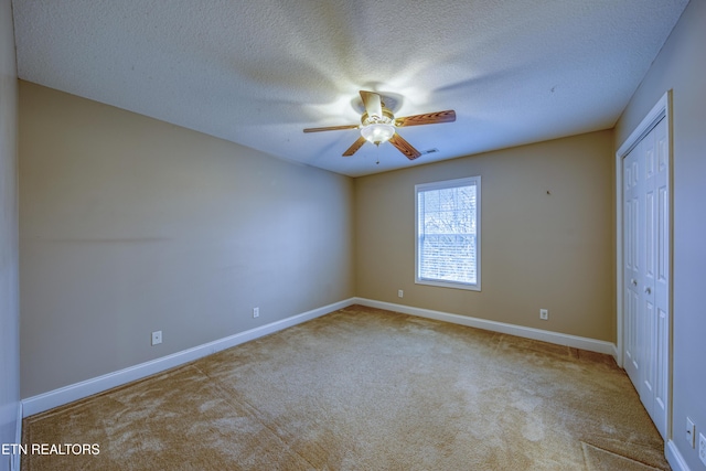 unfurnished bedroom featuring light carpet, a textured ceiling, a closet, and ceiling fan