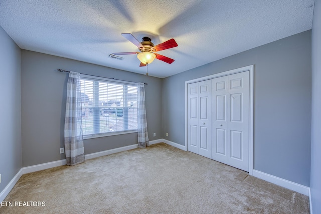 unfurnished bedroom with a textured ceiling, a closet, light colored carpet, and ceiling fan