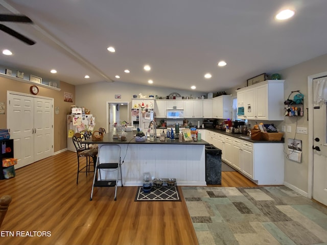 kitchen with lofted ceiling, white cabinets, a kitchen breakfast bar, fridge, and light hardwood / wood-style flooring