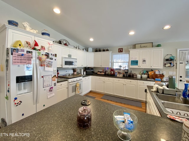 kitchen featuring white cabinetry, lofted ceiling, sink, wood-type flooring, and white appliances