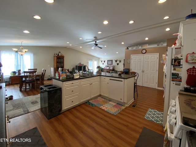 kitchen with vaulted ceiling, dark hardwood / wood-style floors, white cabinets, kitchen peninsula, and white appliances