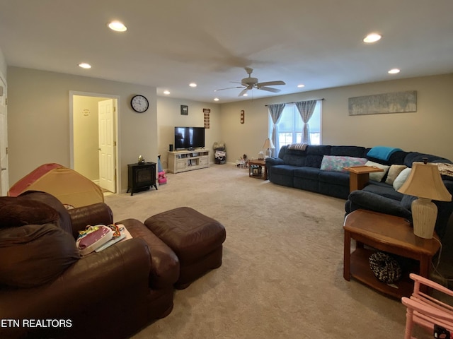 living room with a wood stove, light colored carpet, and ceiling fan