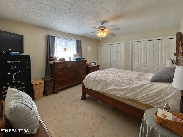 carpeted bedroom with ceiling fan, two closets, and a textured ceiling