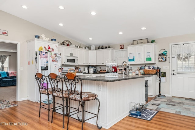 kitchen featuring vaulted ceiling, white microwave, white cabinetry, and a healthy amount of sunlight