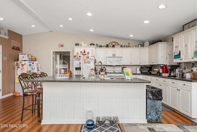 kitchen with vaulted ceiling with beams, a kitchen island with sink, white appliances, a sink, and light wood-style floors