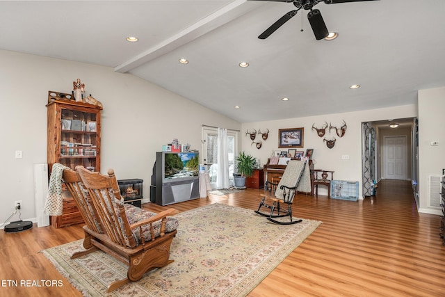 living area with light wood-style floors, recessed lighting, a wood stove, and lofted ceiling with beams