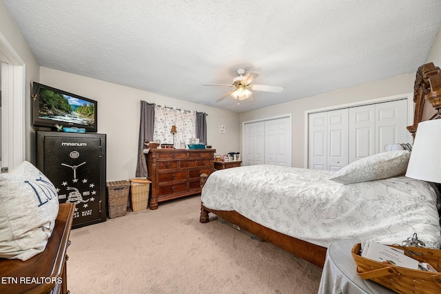 bedroom featuring ceiling fan, a textured ceiling, two closets, and light colored carpet