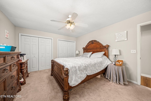 bedroom featuring a textured ceiling, two closets, and light colored carpet