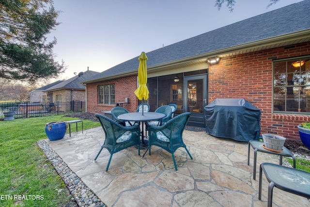 patio terrace at dusk featuring a lawn and area for grilling