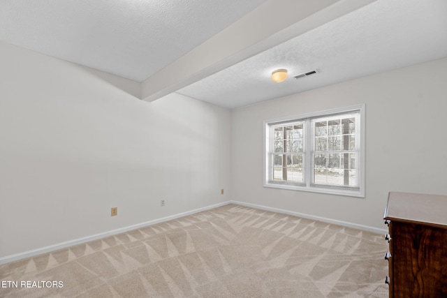 empty room with light carpet, beam ceiling, and a textured ceiling