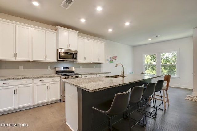 kitchen with white cabinets, sink, appliances with stainless steel finishes, and an island with sink