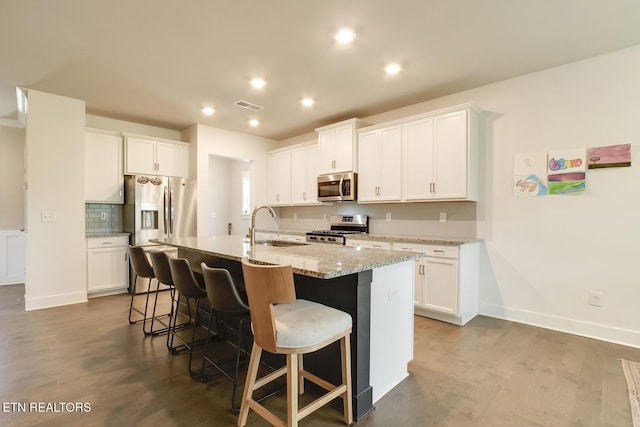 kitchen with a kitchen island with sink, white cabinets, stainless steel appliances, and light stone counters