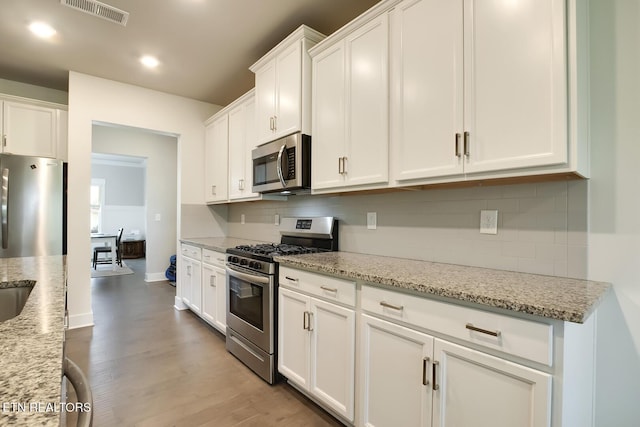 kitchen featuring white cabinets, backsplash, stainless steel appliances, and light stone countertops