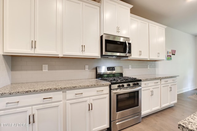 kitchen featuring light stone counters, light hardwood / wood-style flooring, decorative backsplash, white cabinets, and appliances with stainless steel finishes