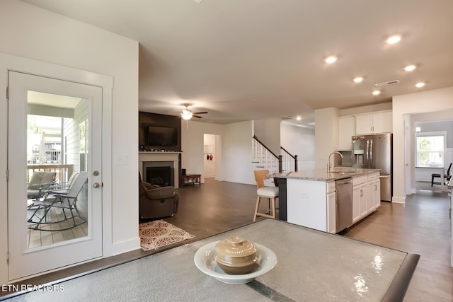 kitchen with light stone countertops, stainless steel appliances, a kitchen island with sink, sink, and white cabinetry