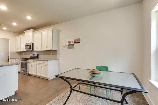 kitchen featuring light stone countertops, white cabinets, stainless steel appliances, and light hardwood / wood-style floors