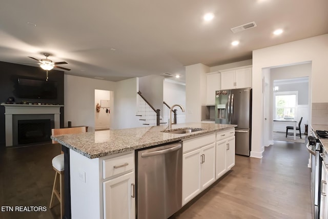 kitchen featuring white cabinets, sink, light stone countertops, an island with sink, and stainless steel appliances