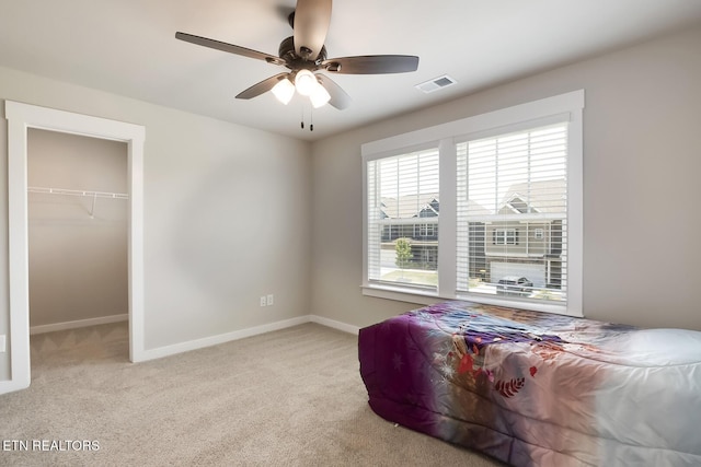 carpeted bedroom featuring a walk in closet, a closet, and ceiling fan