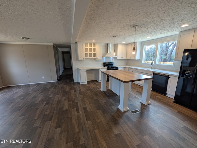 kitchen with wall chimney range hood, decorative light fixtures, white cabinets, and black appliances