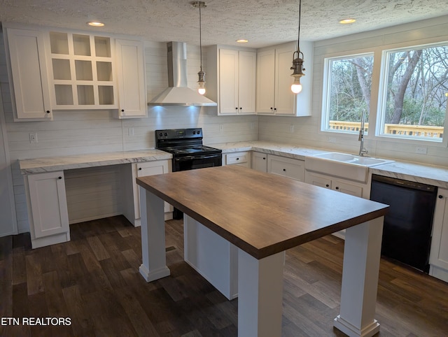 kitchen featuring black appliances, wall chimney exhaust hood, white cabinets, and decorative light fixtures