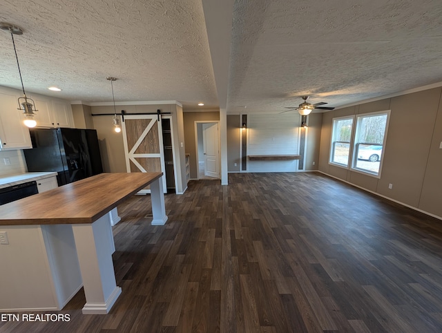 kitchen with black appliances, hanging light fixtures, a barn door, white cabinetry, and butcher block counters