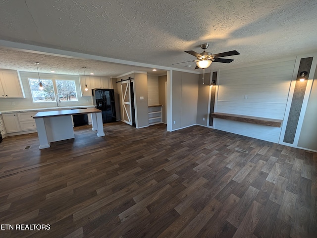 kitchen featuring black fridge with ice dispenser, ceiling fan, a barn door, white cabinets, and a center island