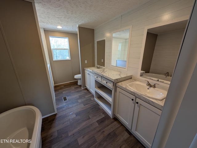 bathroom with a washtub, wood-type flooring, a textured ceiling, toilet, and vanity