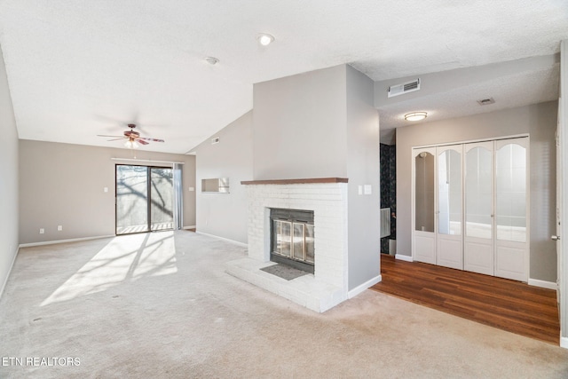 unfurnished living room featuring a brick fireplace, a textured ceiling, light colored carpet, and vaulted ceiling