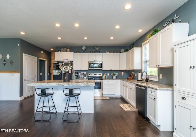 kitchen with stainless steel appliances, dark hardwood / wood-style flooring, a kitchen island, white cabinets, and sink