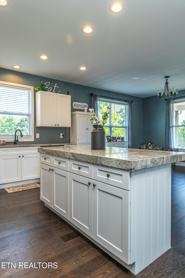 kitchen with a notable chandelier, dark hardwood / wood-style flooring, a kitchen island, white cabinets, and sink