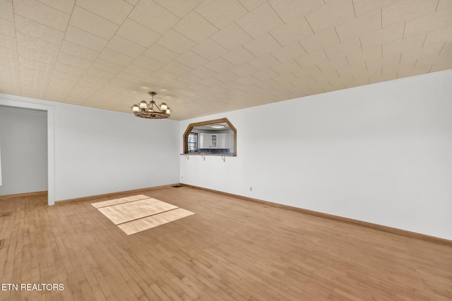 empty room featuring light wood-style floors, a notable chandelier, and baseboards